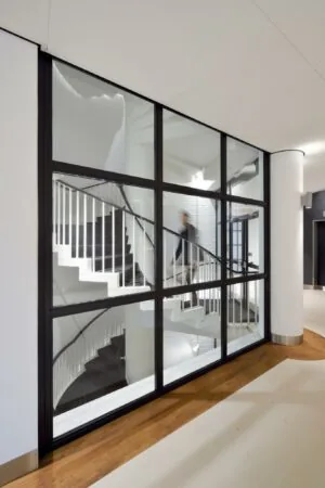 Doorkijk op een modern trappenhuis met witte wenteltrap achter een glazen wand in het gebouw aan de Floris Grijpstraat.